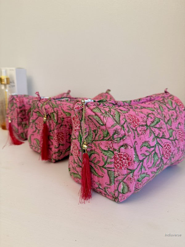 Three pink fabric cosmetic pouches with a green floral block print and red tassels, arranged on a light surface against a plain off-white background | Rose Garden