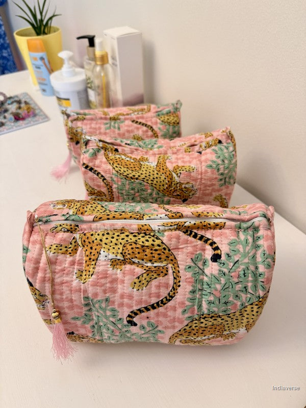 Three quilted cosmetic pouches with a pink and green botanical print and cheetah pattern, arranged on a white tabletop with skincare items in the background | Rose Leopard