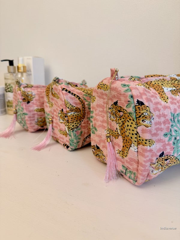 Three pink zippered cosmetic pouches with a leopard print pattern and pink tassels, arranged on a light beige surface against a plain wall | Rose Leopard