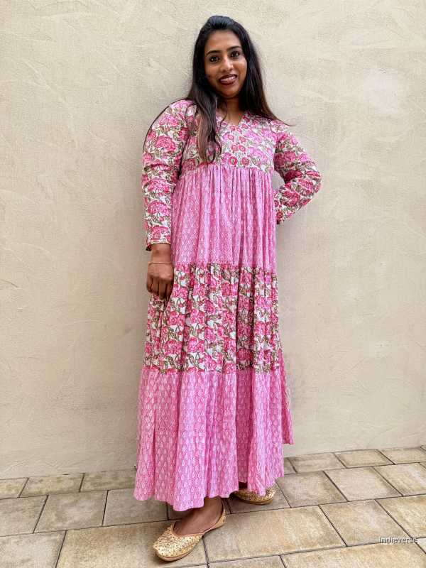 Woman wearing a pink floral dress standing against a beige wall.