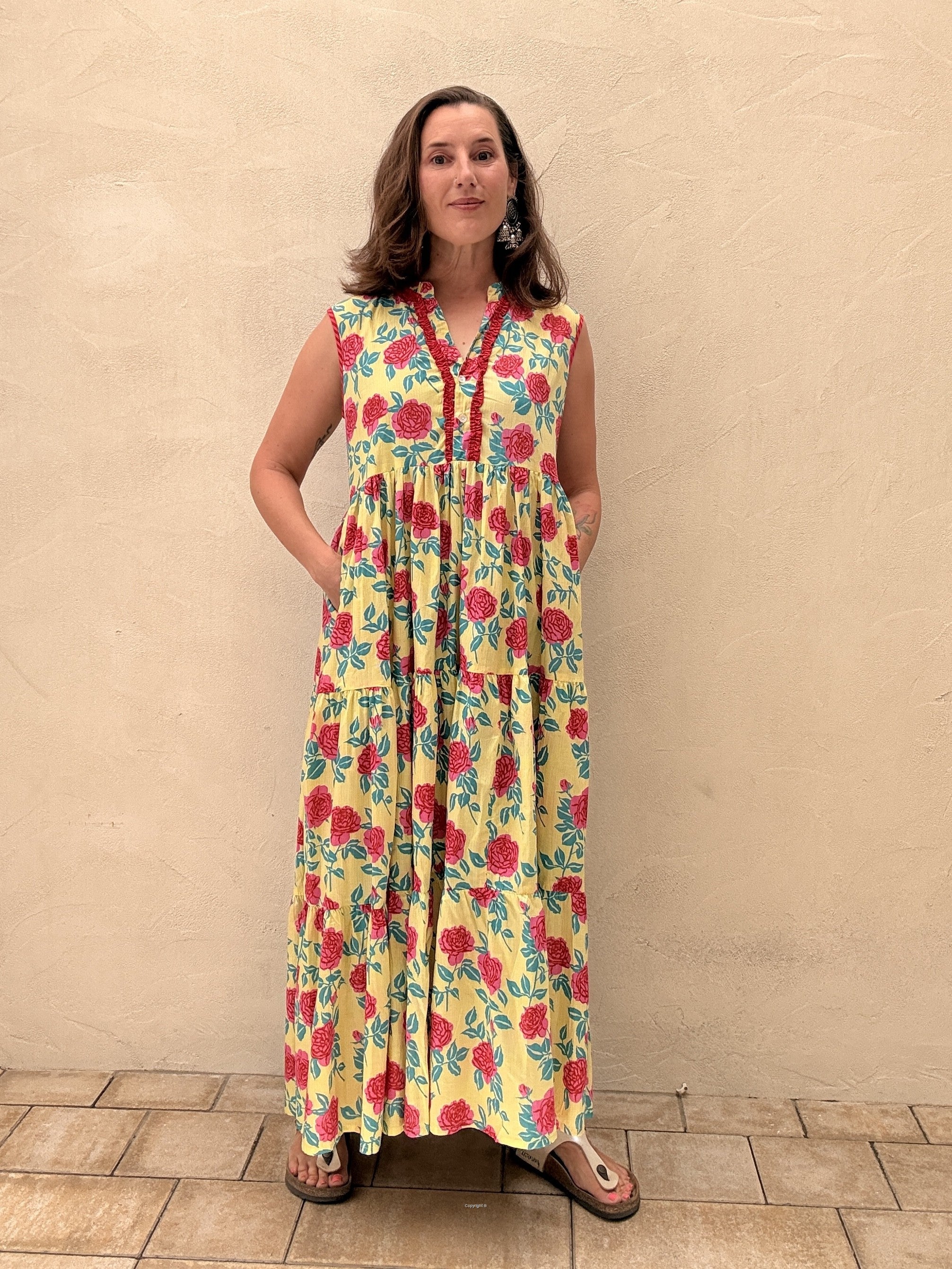 Woman wearing a colorful floral dress against a beige wall.