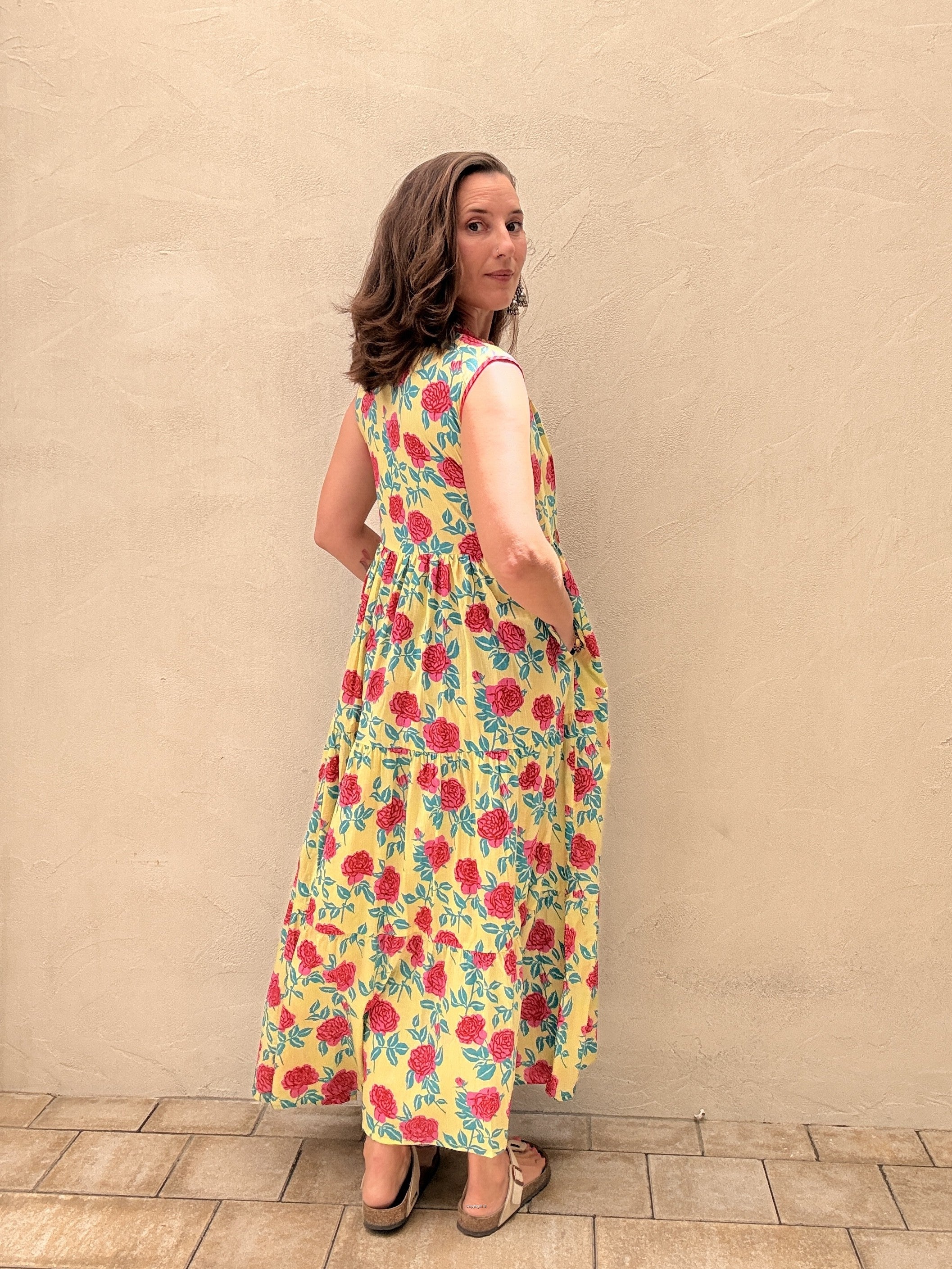 Woman wearing a sleeveless long dress with rose design standing in front of a beige wall