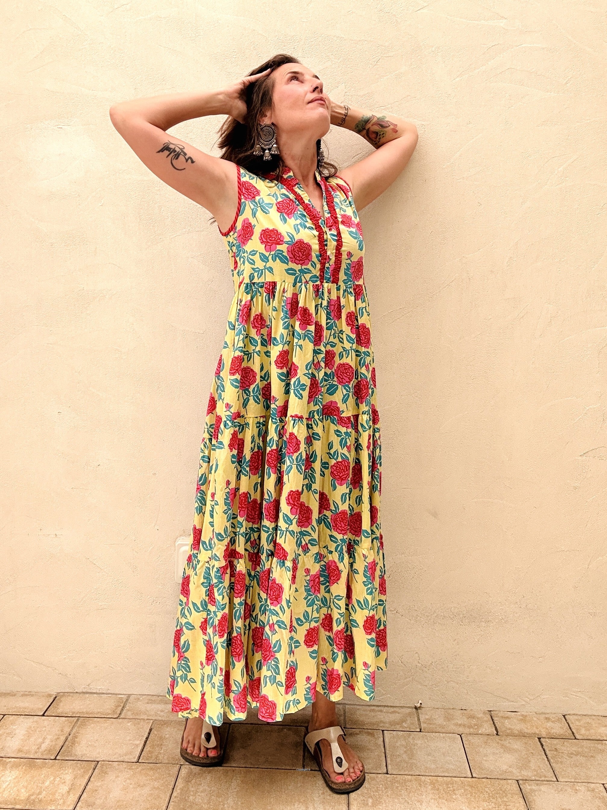 Woman wearing a yellow floral dress against a beige wall.