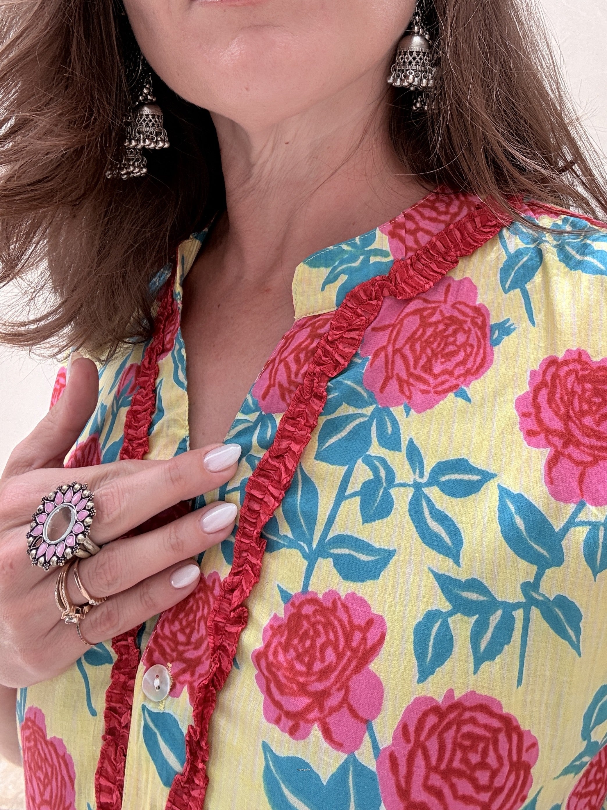 Close-up of a person wearing a floral dress with red trim and jewelry.