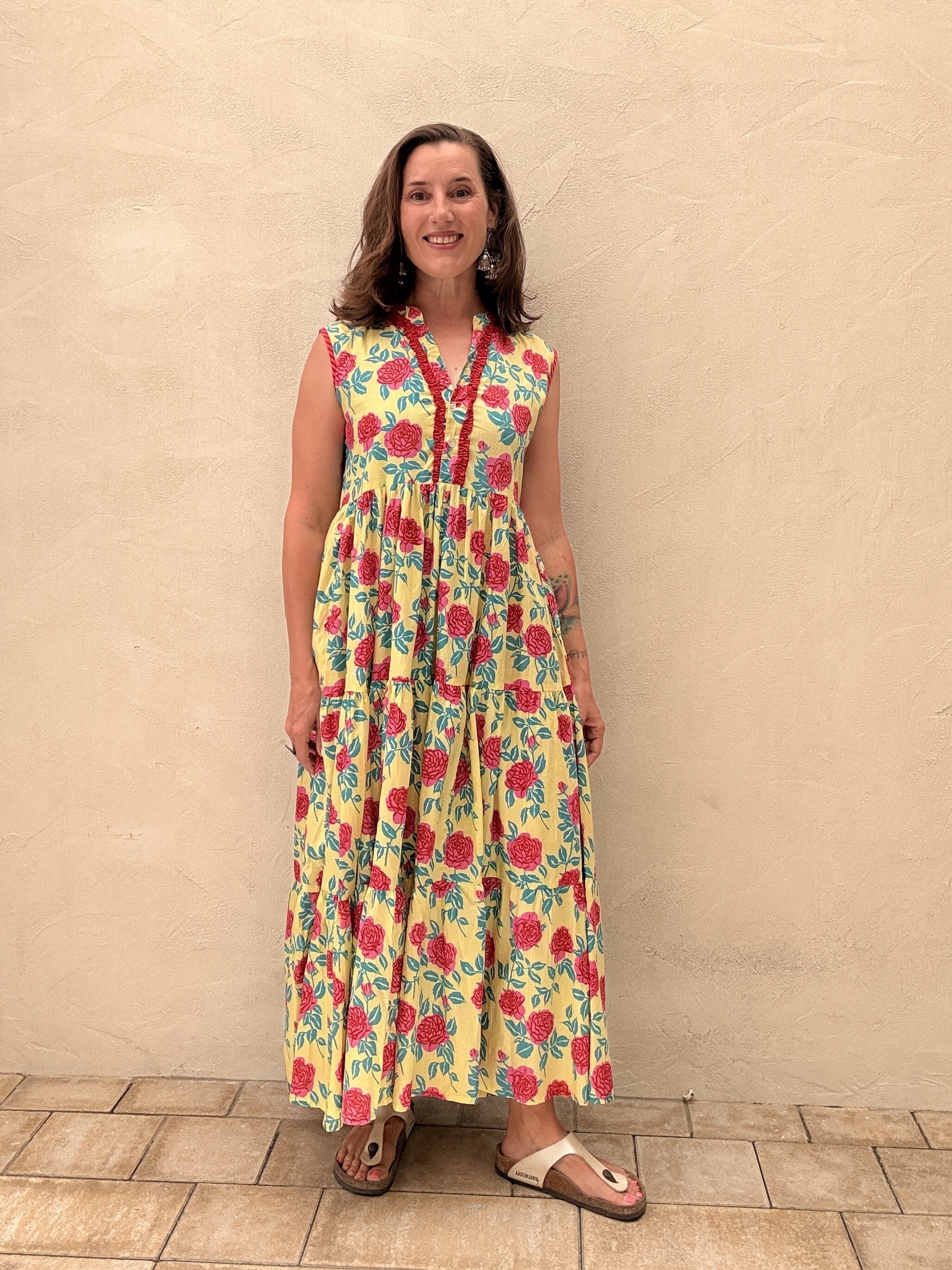 Woman wearing a colorful floral dress against a beige wall.