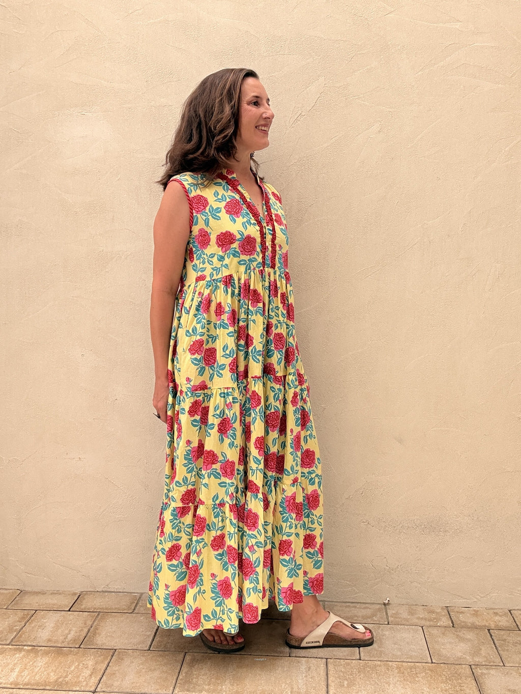 Woman wearing a floral dress standing against a beige wall.