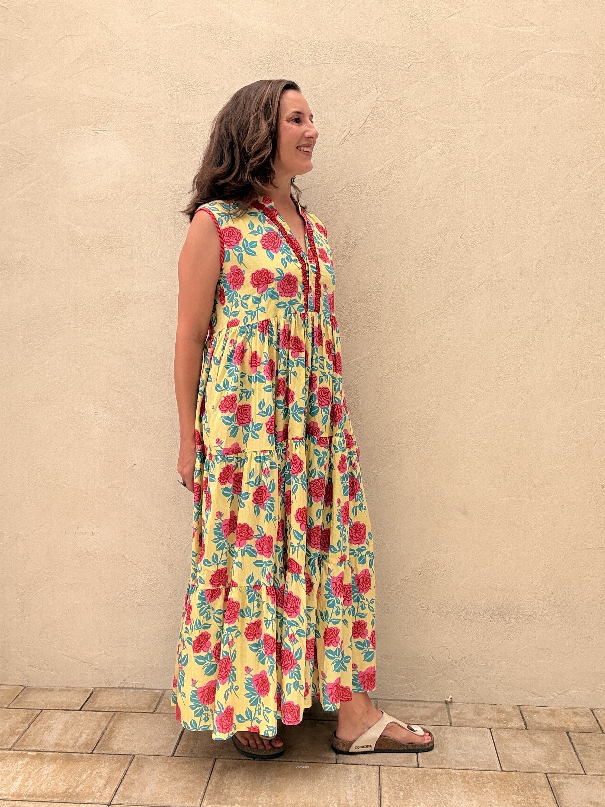 Woman wearing a floral dress standing against a beige wall.