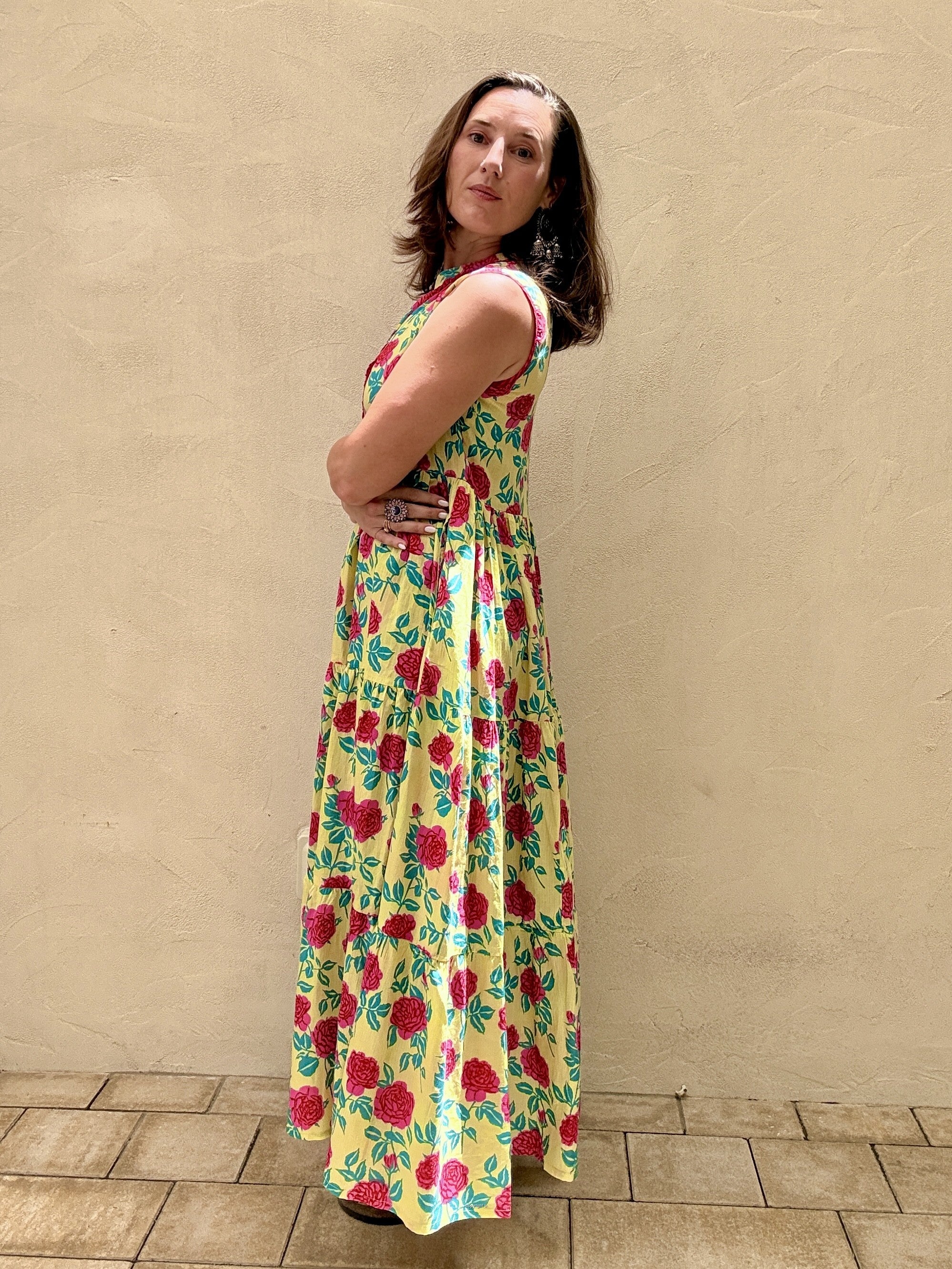 Woman wearing a colorful floral dress against a beige wall.