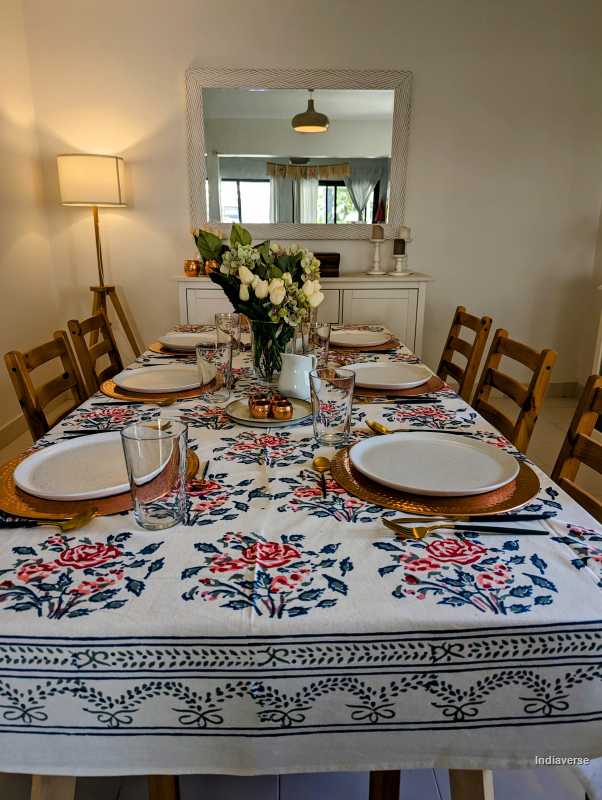 Dining table set with floral tablecloth, plates, and cutlery in a room with a mirror and lamp.