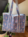 Blue patterned tote bag with striped handles on a wooden surface.