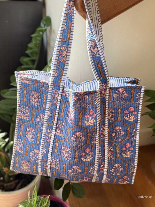 Blue patterned tote bag with striped handles on a wooden surface.