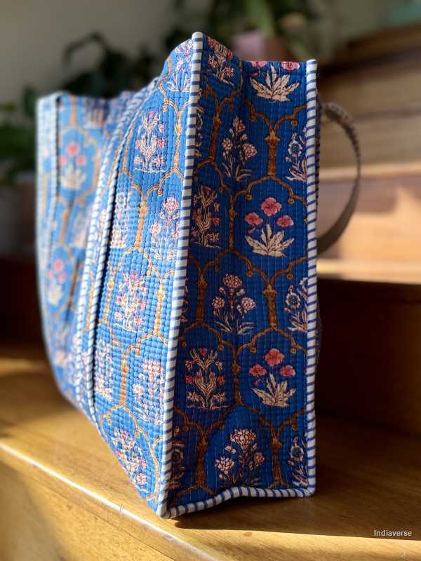 Blue embroidered cotton tote bag on a wooden surface with a blurred background
