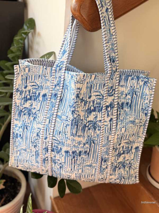 Blue and white patterned tote bag hanging on a wooden surface with plants in the background.