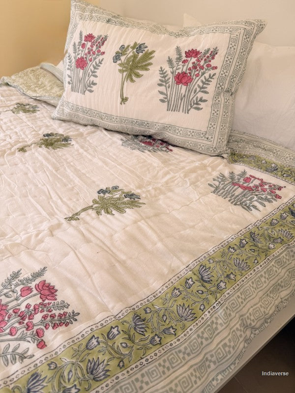Single cotton quilt with two matching pillow cases and red flower design arranged on a white bed frame