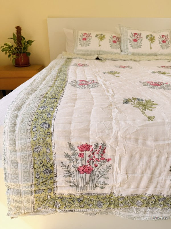 Single cotton quilt with two matching pillow cases and red flower design arranged on a white bed frame