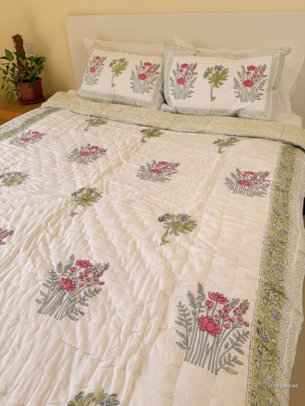 Single cotton quilt with two matching pillow cases and red flower design arranged on a white bed frame