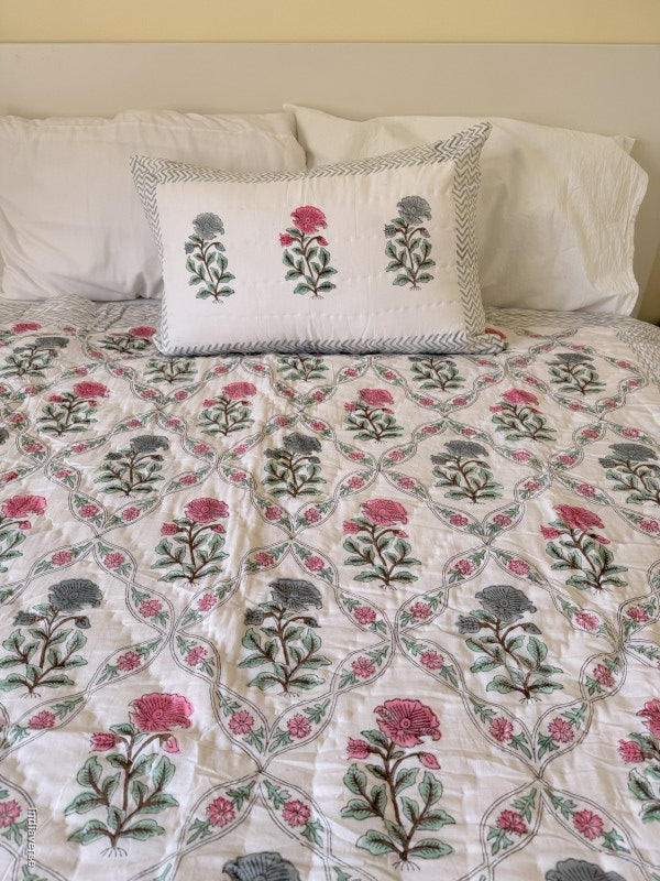 quilted cotton blanket with geometrically arranged floral design of blue and red flowers draped over a bed with one matching pillowcase