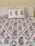 quilted cotton blanket with geometrically arranged floral design of blue and red flowers draped over a bed with one matching pillowcase