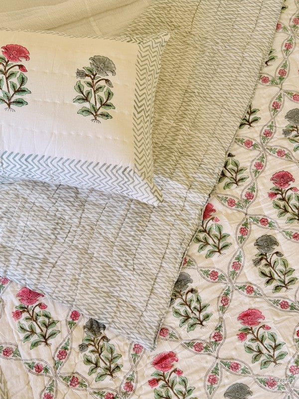 quilted cotton blanket with geometrically arranged floral design of blue and red flowers draped over a bed with one matching pillowcase