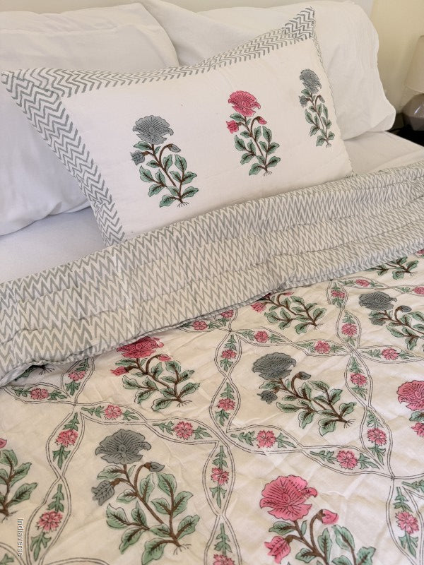 quilted cotton blanket with geometrically arranged floral design of blue and red flowers draped over a bed with one matching pillowcase
