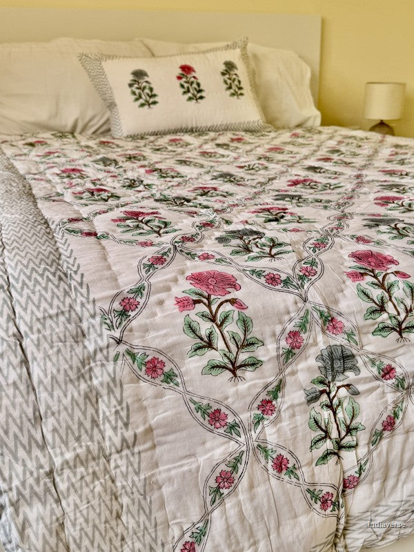 quilted cotton blanket with geometrically arranged floral design of blue and red flowers draped over a bed with one matching pillowcase