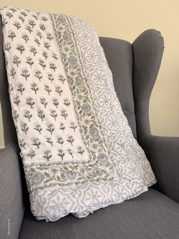 quilted blanket folded on an arm chair showing a grey geometric pattern on the border and reverse side and on the front small blue and green flowers