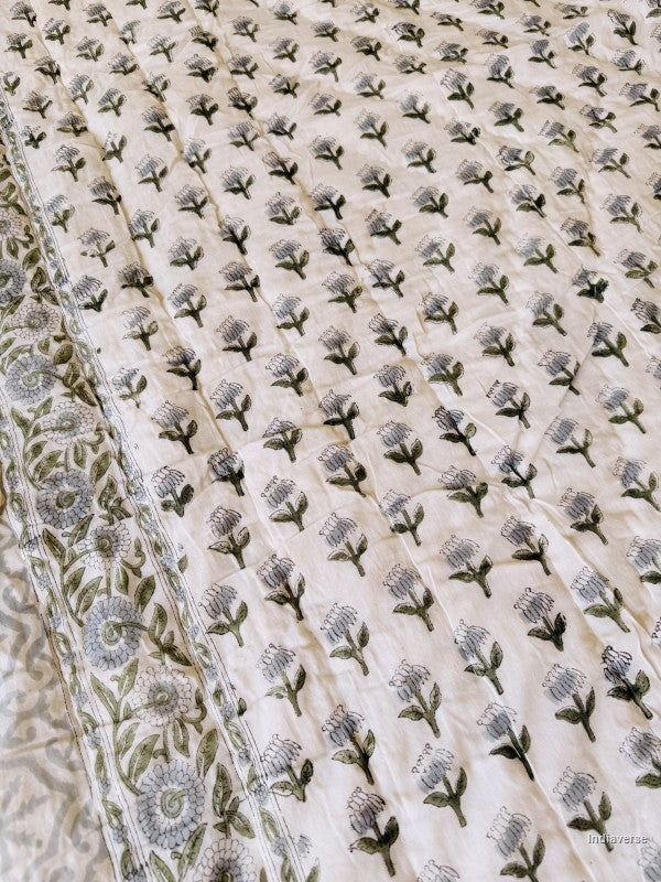 Close up of the floral pattern of small grey and green flowers on a white quilted blanket