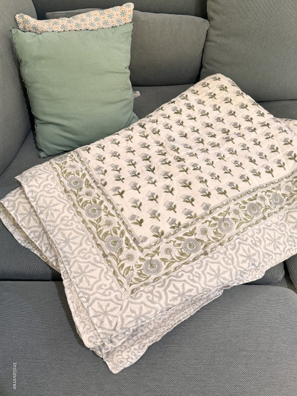 quilted blanket with floral design on a grey couch with pillows in the corner folded so the grey geometric border is showing