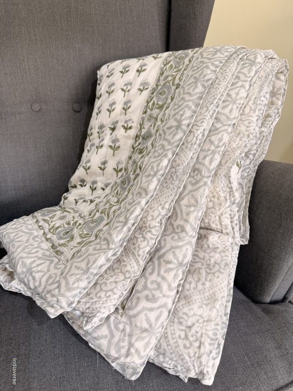 quilted blanket folded on an arm chair showing a grey geometric pattern on the border and reverse side and on the front small blue and green flowers