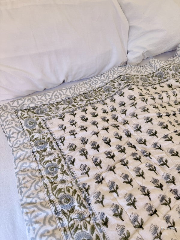 White quilted blanket with small grey floral design arranged on a bed with white pilllowcases