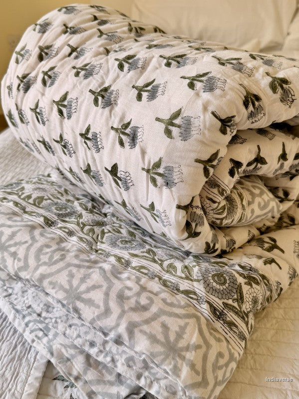 Rolled up white single quilt with blue and grey floral pattern and grey geometric border