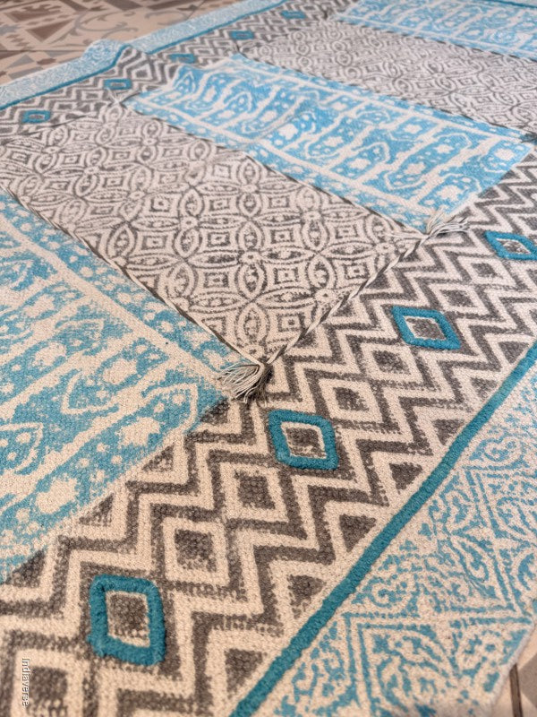 A close-up of a patterned area rug with geometric and tribal-inspired designs in blue, gray, and cream.