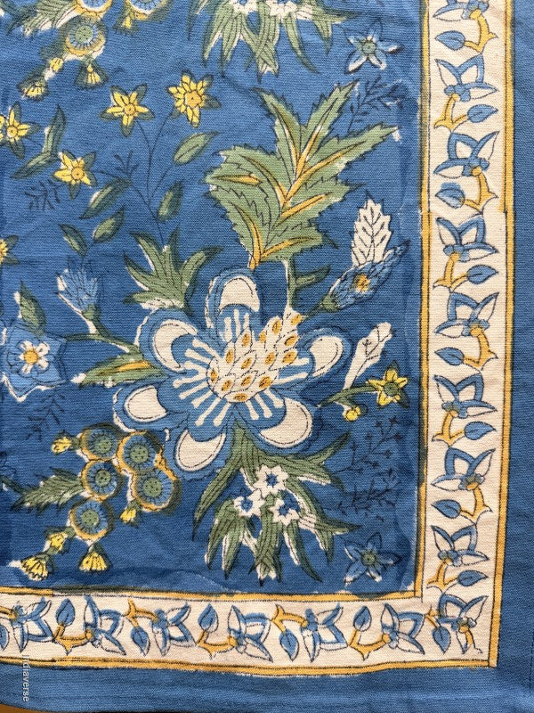 A close-up of a blue patterned textile or rug showing a floral design with cream, green, and yellow elements, plus a decorative border.