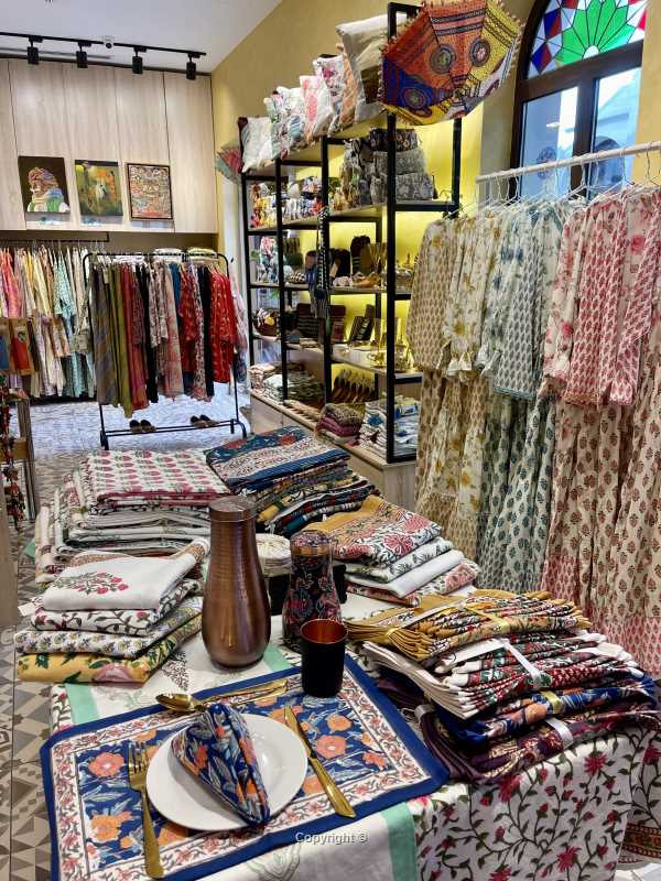 View at tableware collection with placemats, table cloth and copper bottles and maxi dresses for women next to it