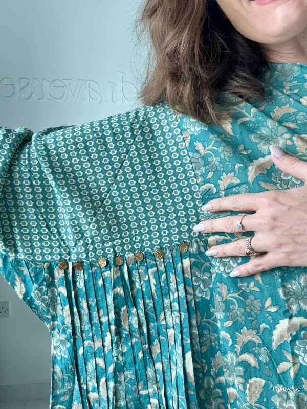 Teal patterned dress with pleated details worn by a person against a light blue background