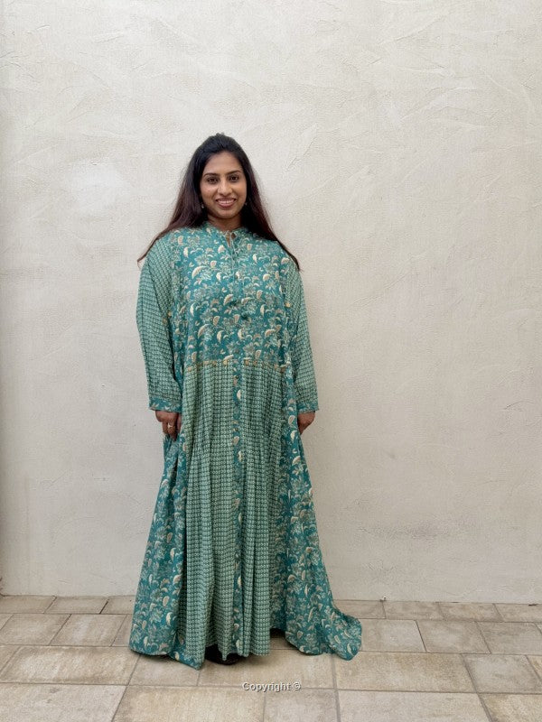 Woman wearing a green patterned dress standing against a plain wall.