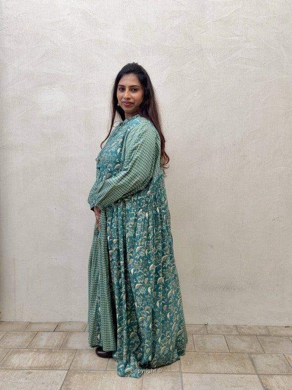 Woman wearing a green patterned outfit standing against a plain wall.