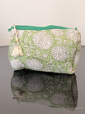 toiletry bag with a tassel in green with white flowers sitting on a glass surface