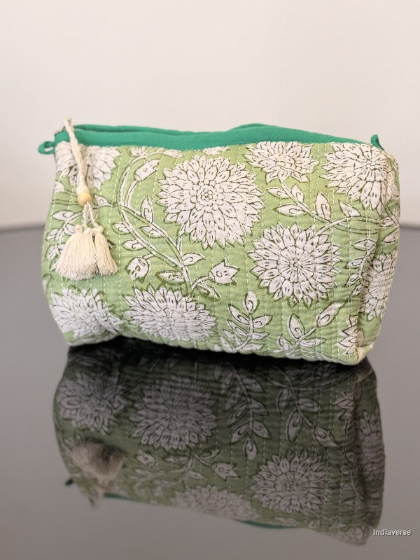 toiletry bag with a tassel in green with white flowers sitting on a glass surface