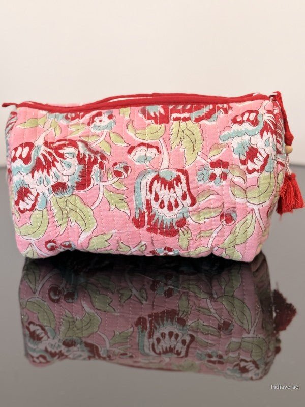 Pink floral fabric pouch with a red zipper on a reflective surface.