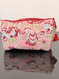 Pink floral fabric pouch with a red zipper on a reflective surface.
