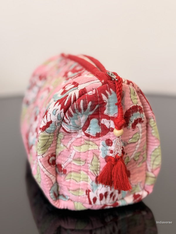 Decorative fabric pouch with floral pattern and red tassel on a reflective surface.