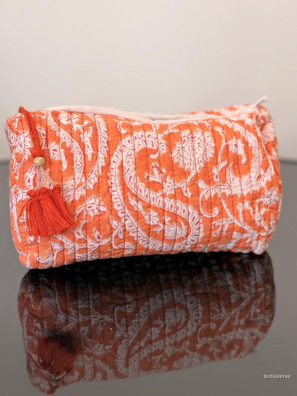 orange toiletry bag with tassels sitting on a glass surface