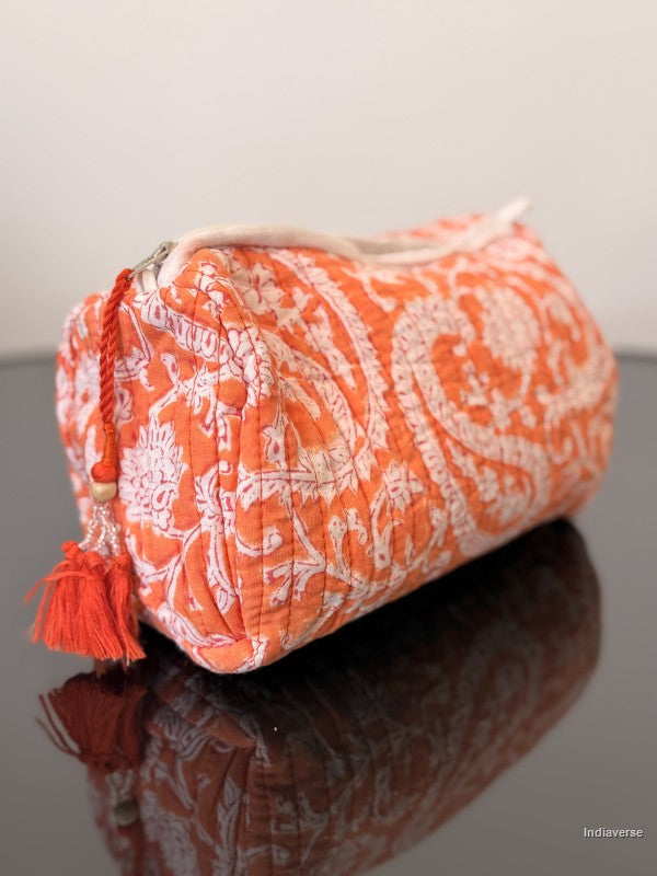 Orange and white patterned pouch with a tassel on a reflective surface