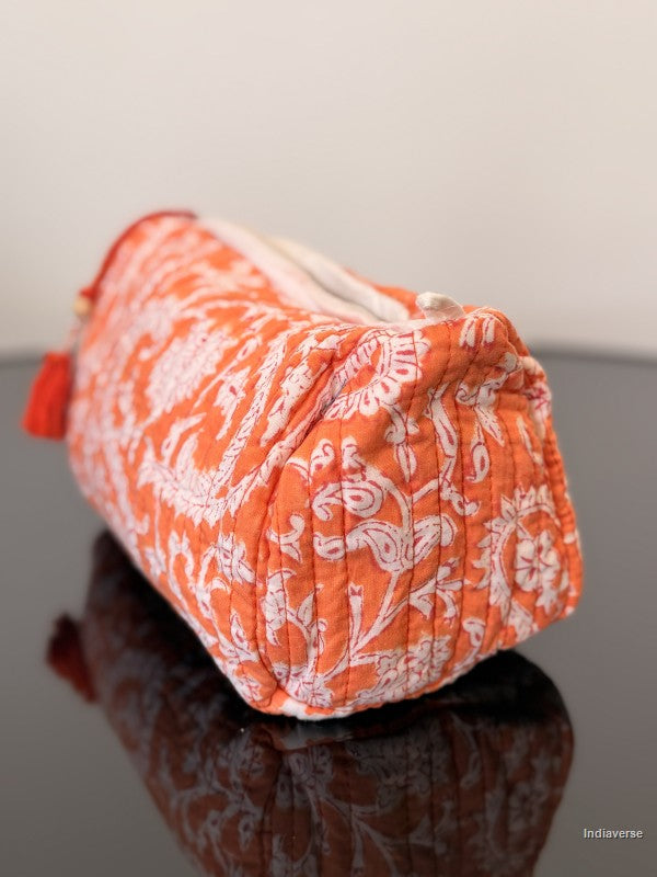 orange toiletry pouch with floral pattern sitting on a glass surface