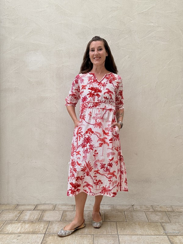 Woman wearing a red and white floral dress standing against a beige wall.