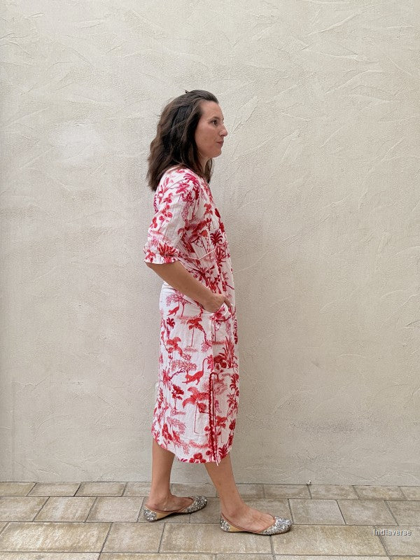 Woman wearing a red floral dress standing against a plain wall.