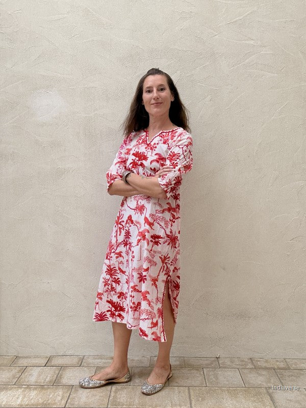 Woman wearing a red floral dress standing against a beige wall.