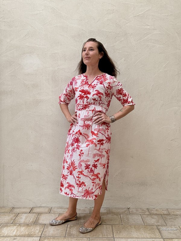 Woman wearing a red floral dress against a beige wall.