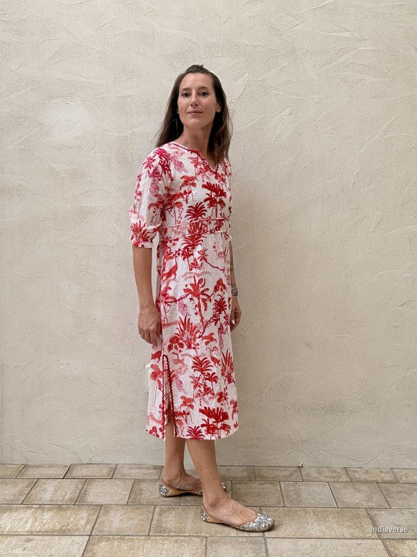 Woman wearing a red floral dress standing against a beige wall.